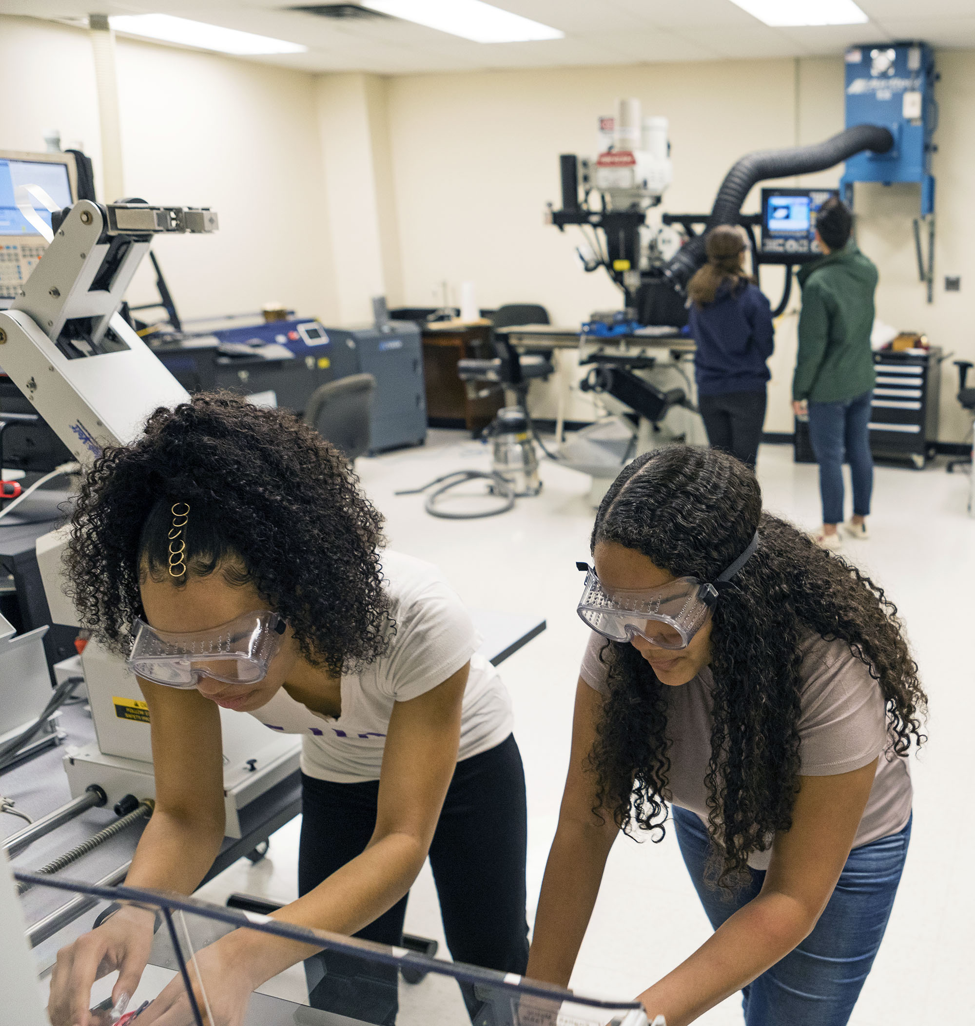Two female students wear goggles and work in an engineering lab.