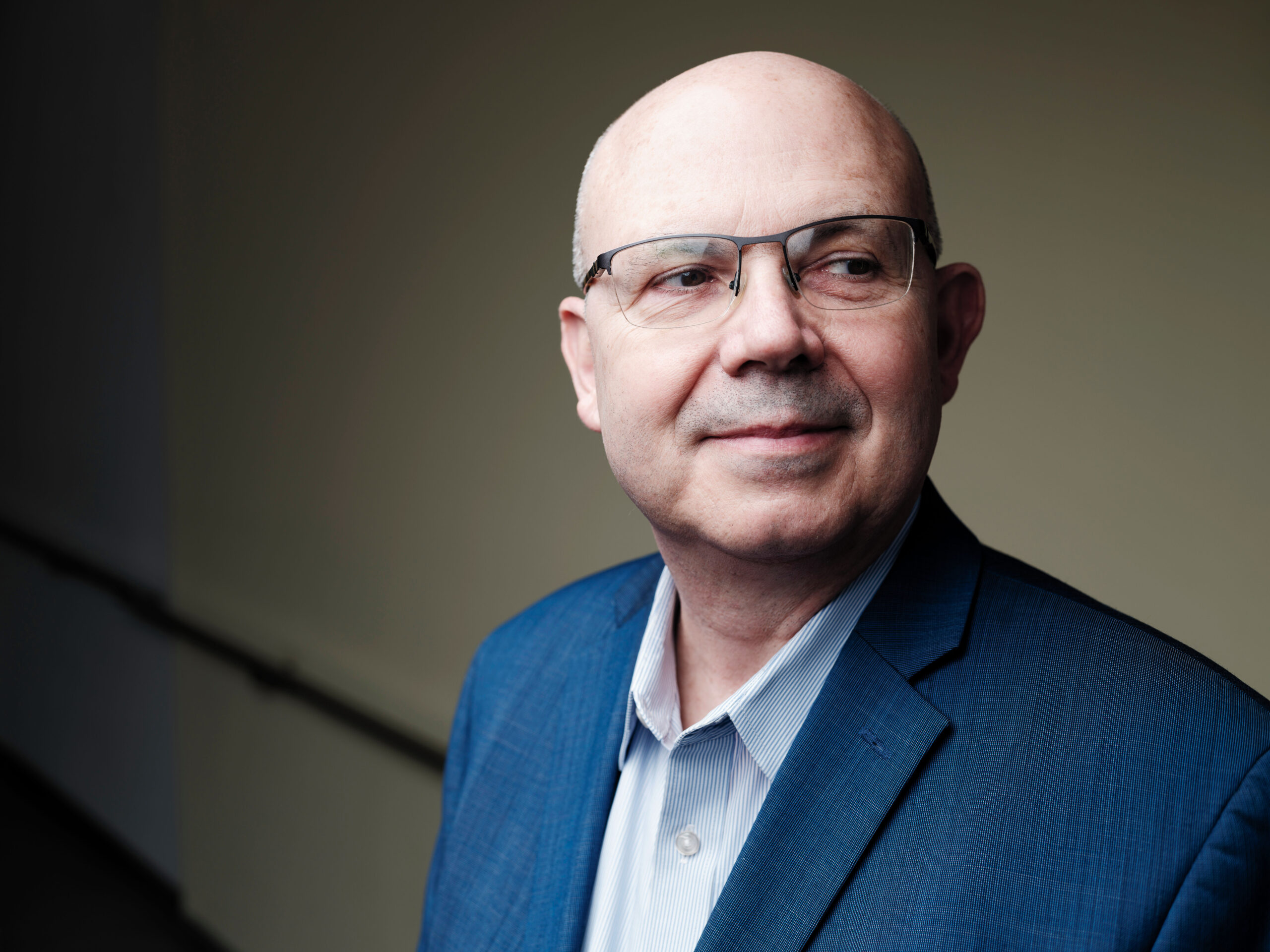 Portrait of a bald man wearing glasses and a sports jacket. He is looking off into the distance.