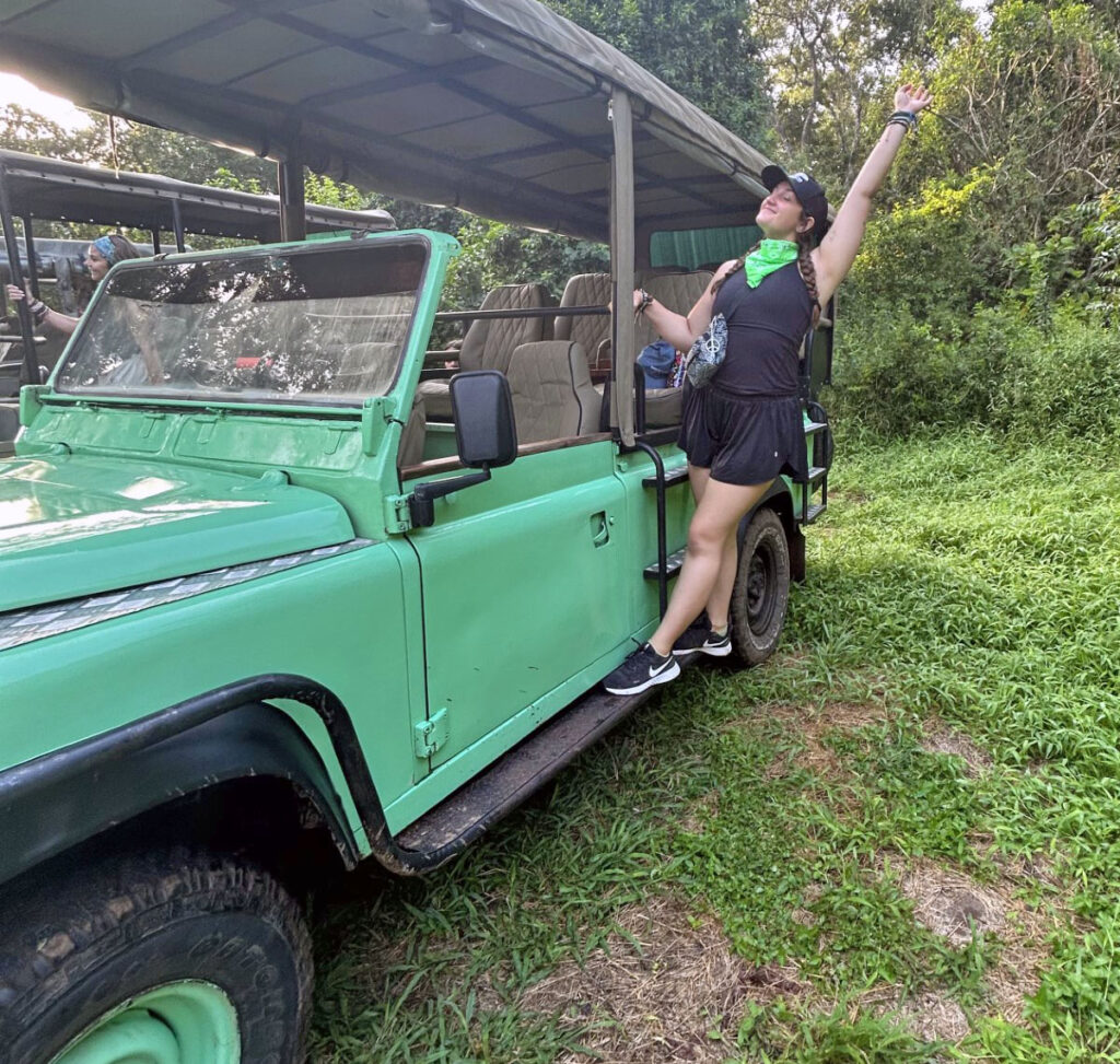 A young woman hangs off of a stopped safari truck near Nyerere National Park in Tanzania.