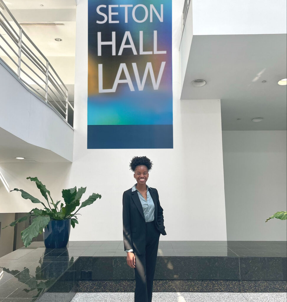 A young woman stands below a Seton Hall Law school banner in an atrium.