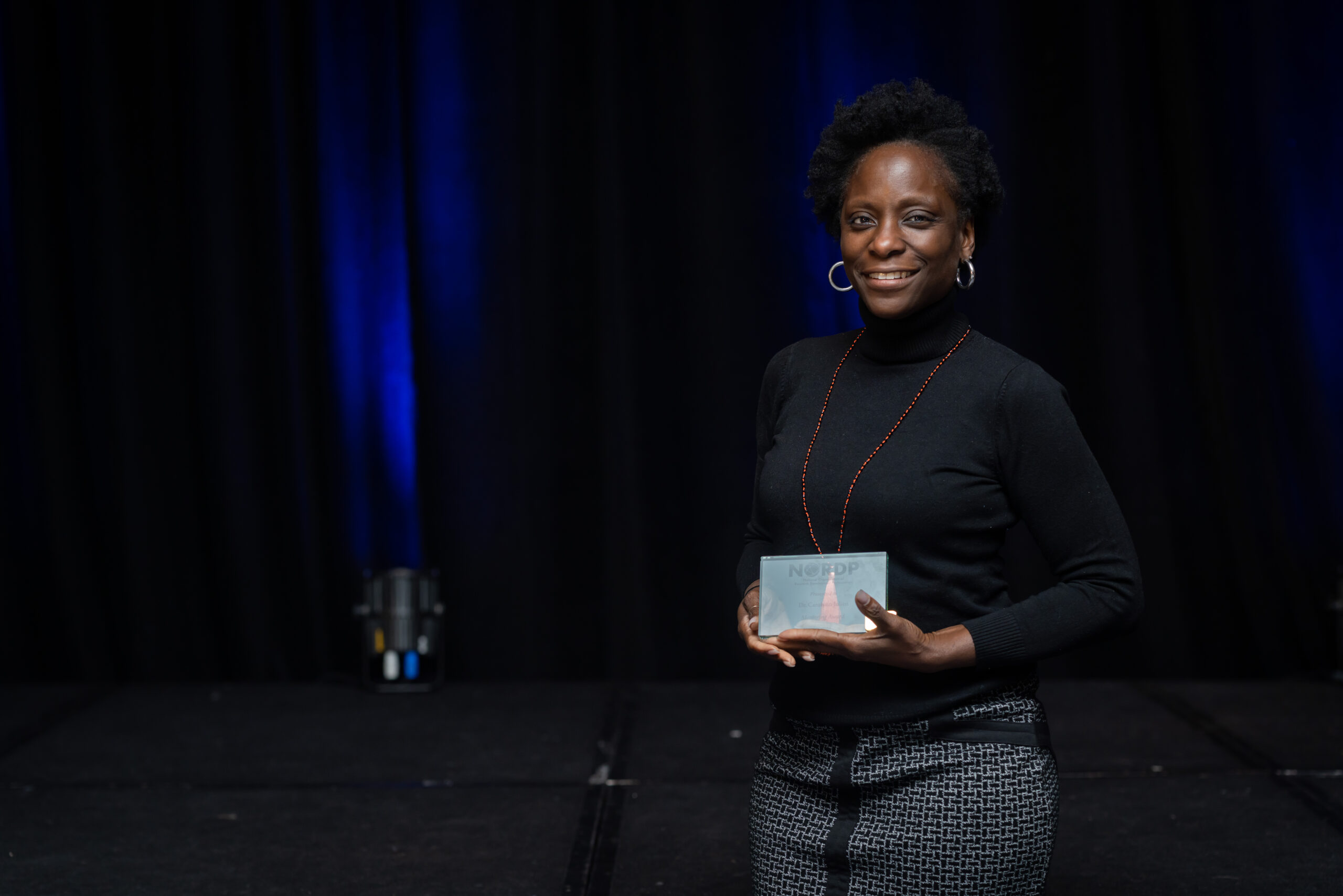 A woman stands, holding her award.