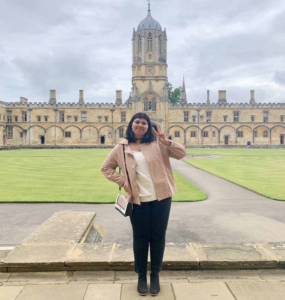 A young woman poses for a photo in front of a grand building in Oxford, England.