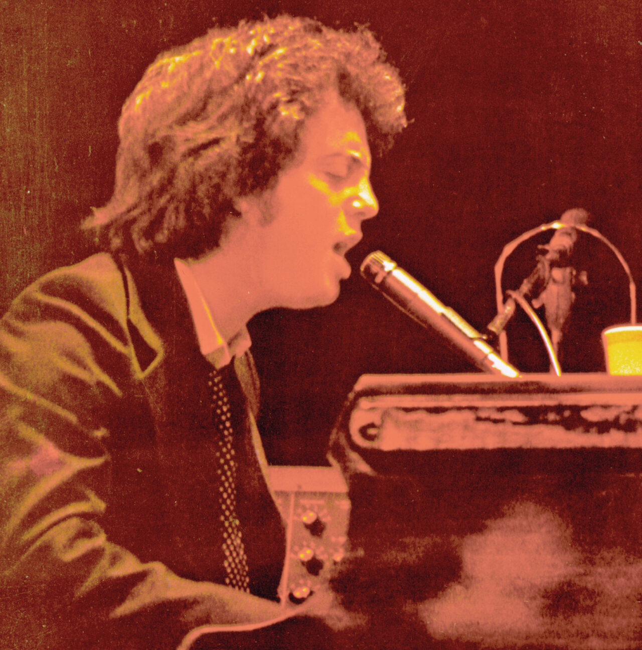 A man sits playing a piano and singing into a microphone.