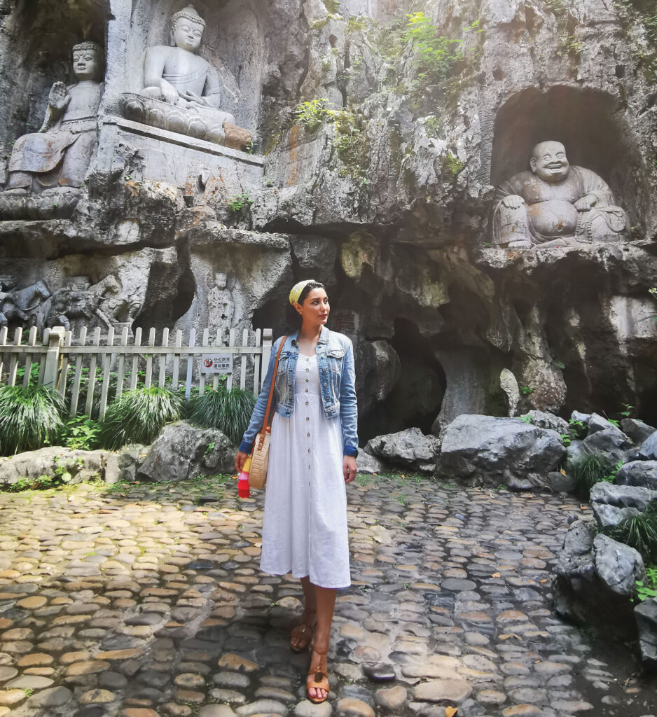 A young woman stands among statues on cobblestones.