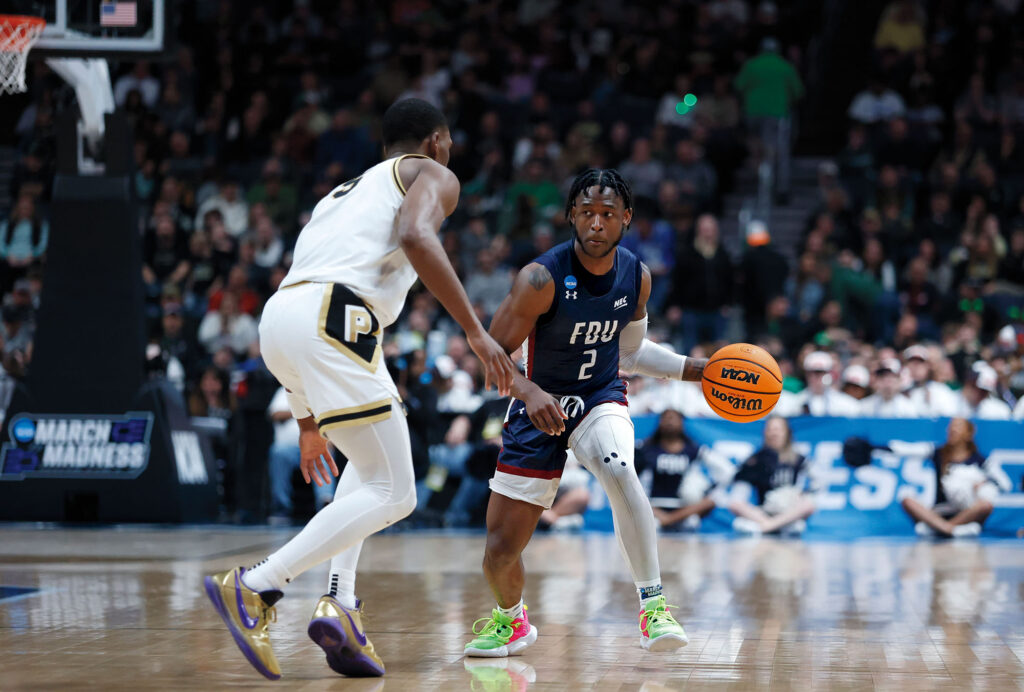 An FDU Knights player, #2, wearing a navy blue jersey, has the basketball against Purdue.