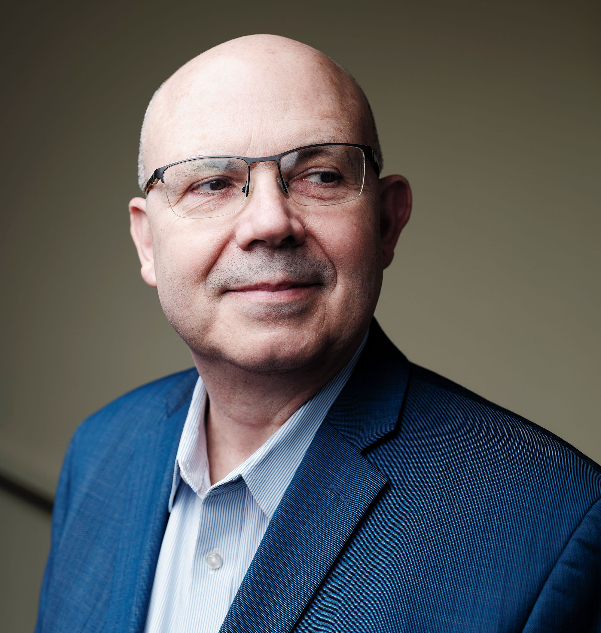 Portrait of a bald man wearing glasses and a sports jacket. He is looking off into the distance.