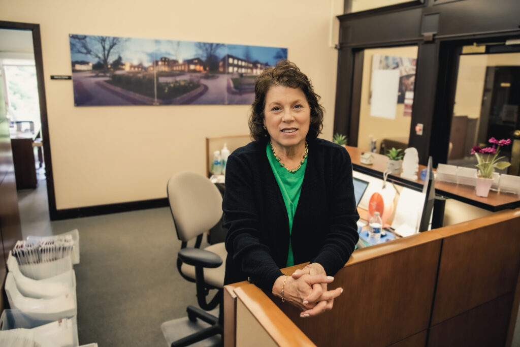 A woman leans on her cubicle, her hands are folded together.