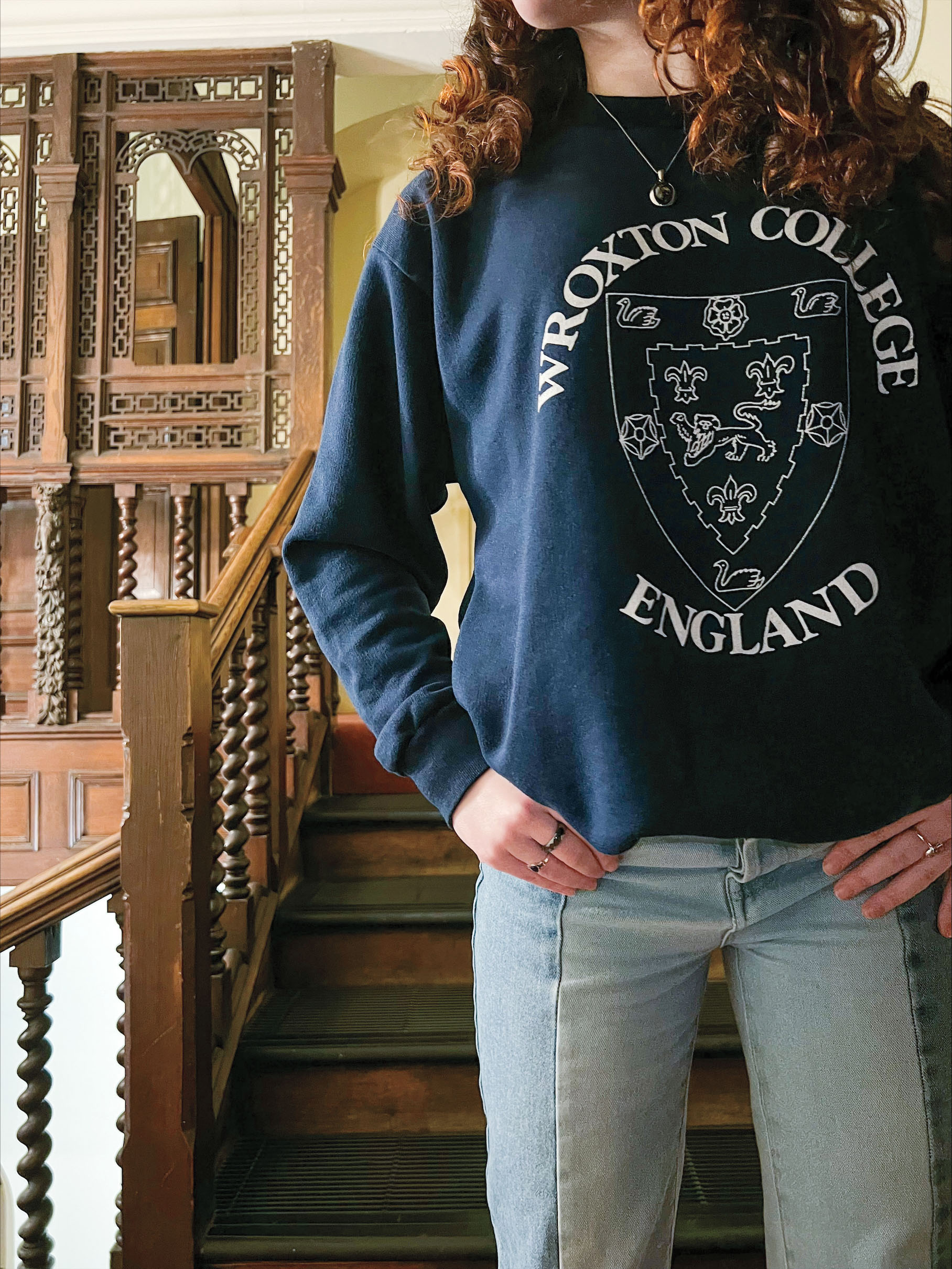 A close-up photo of a young woman wearing a vintage Wroxton College sweatshirt.