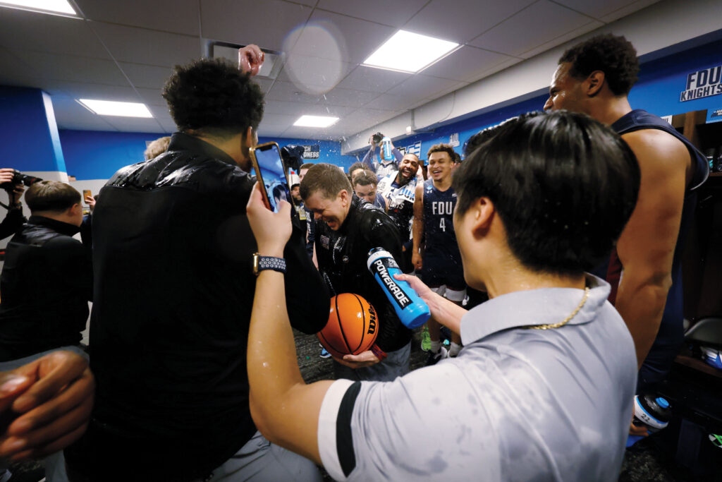 A group of men cheer and spray water in excitement after winning a basketball game. 