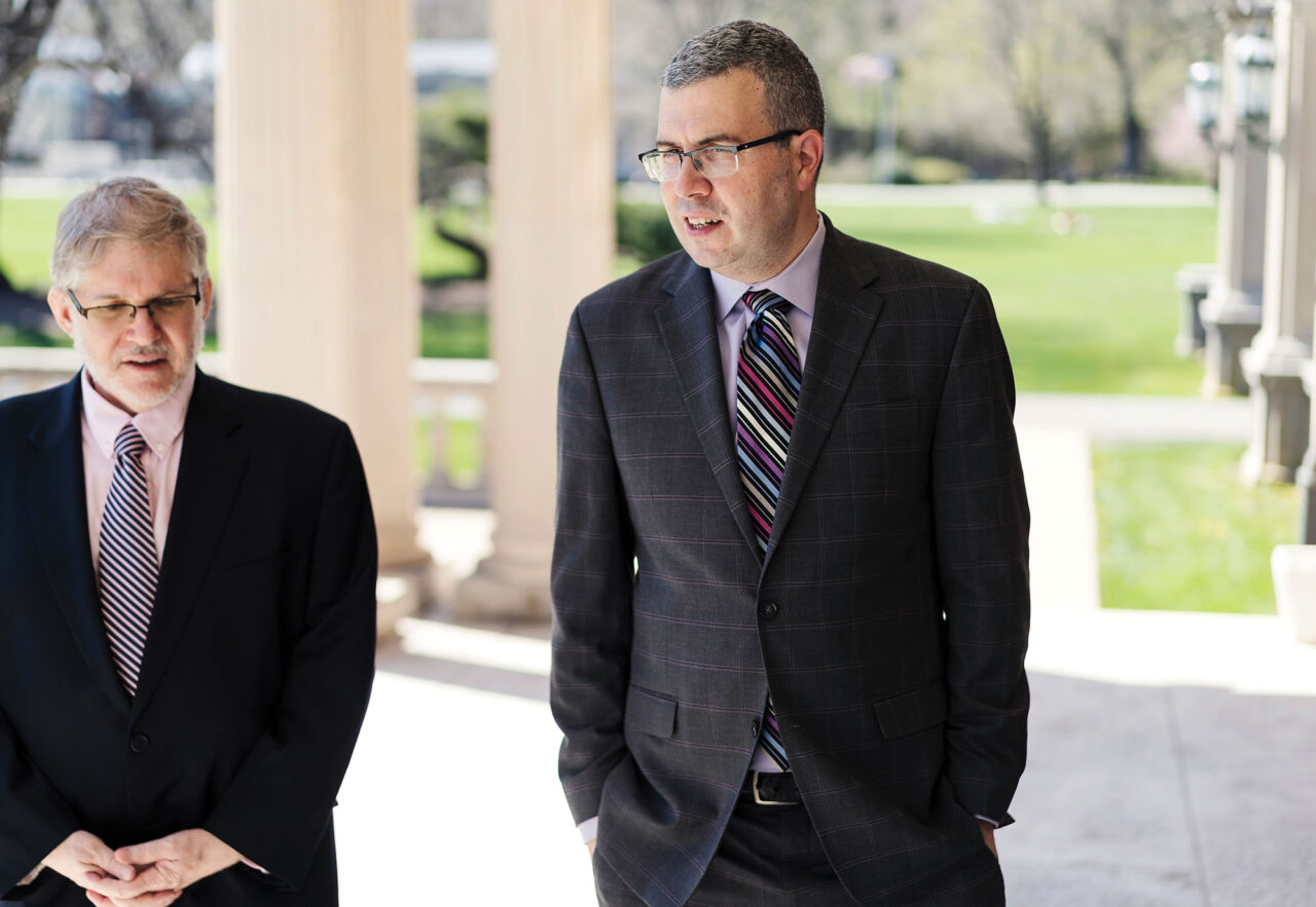 Two men in suits walk and talk outside.