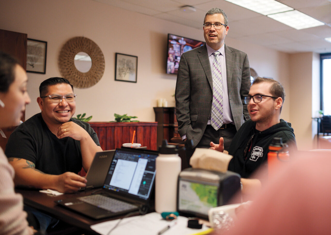 A man in suit stands chatting with students who are studying for finals.