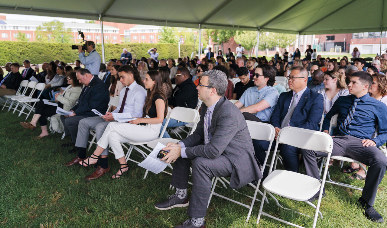 People sit in folding chairs at an outdoor awards reception.