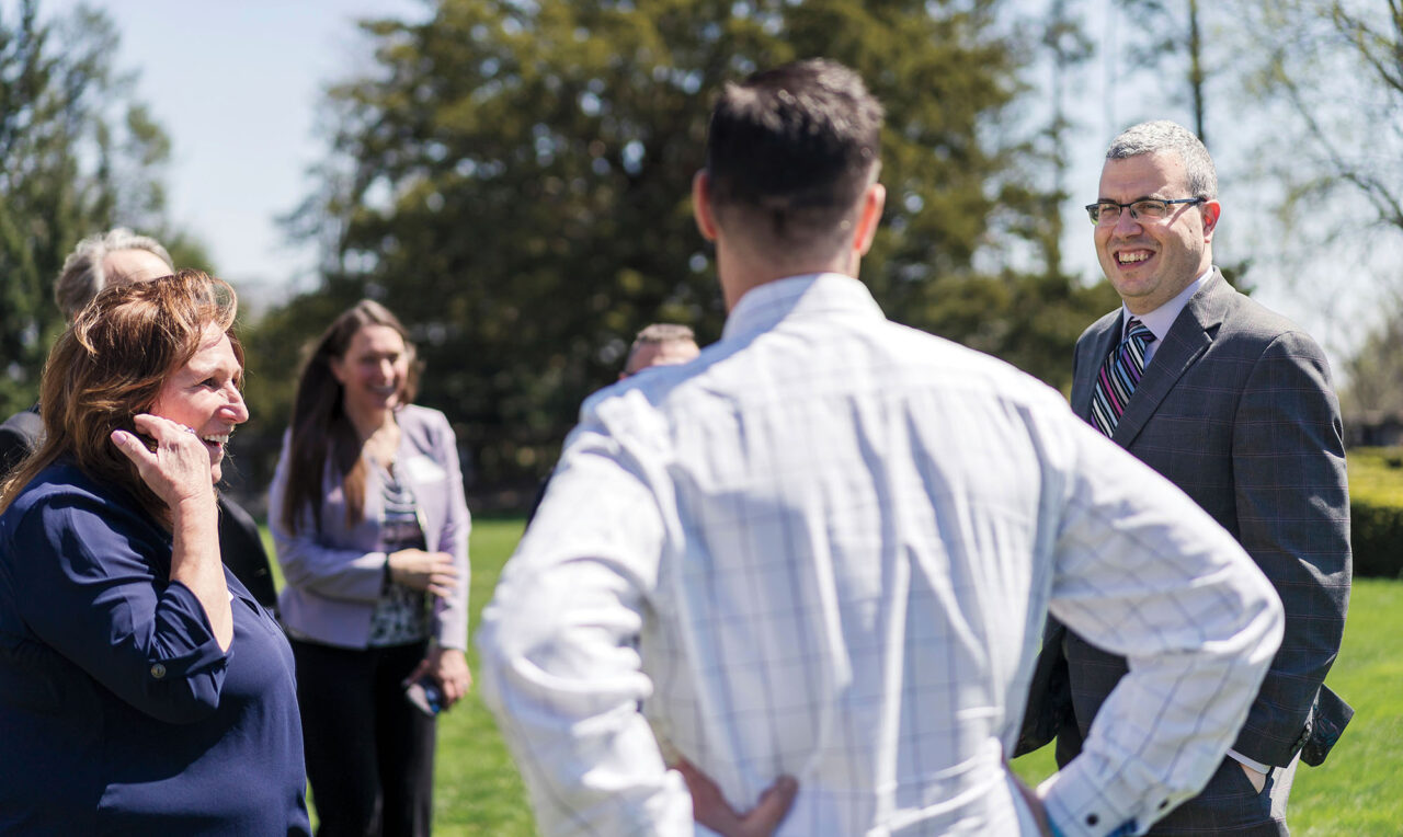 A group of people stand in a circle outside and chat.