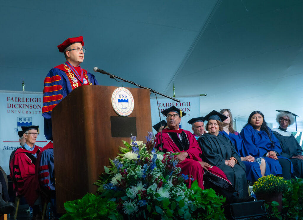 A man in academic regalia stands at a podium on stage.