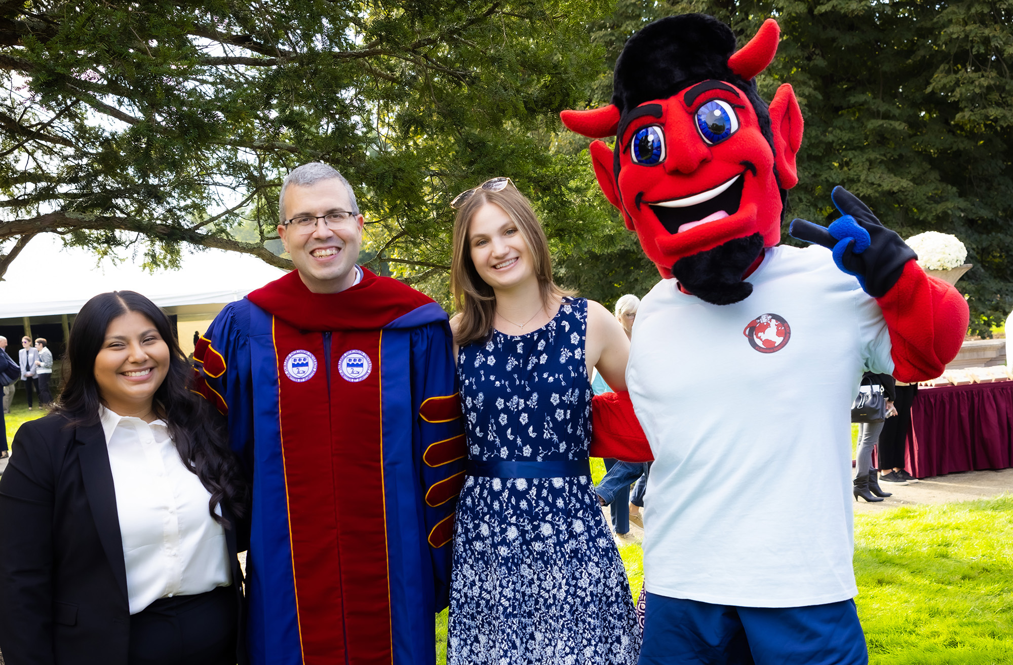 Two young women and a man pose for a photo with a Devil mascot.