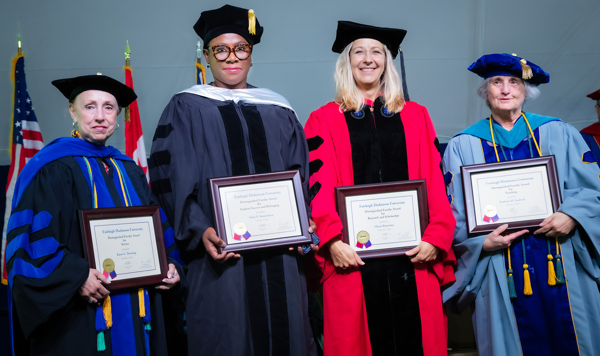 Four women dressed in academic regalia hold awards and pose for a photo.