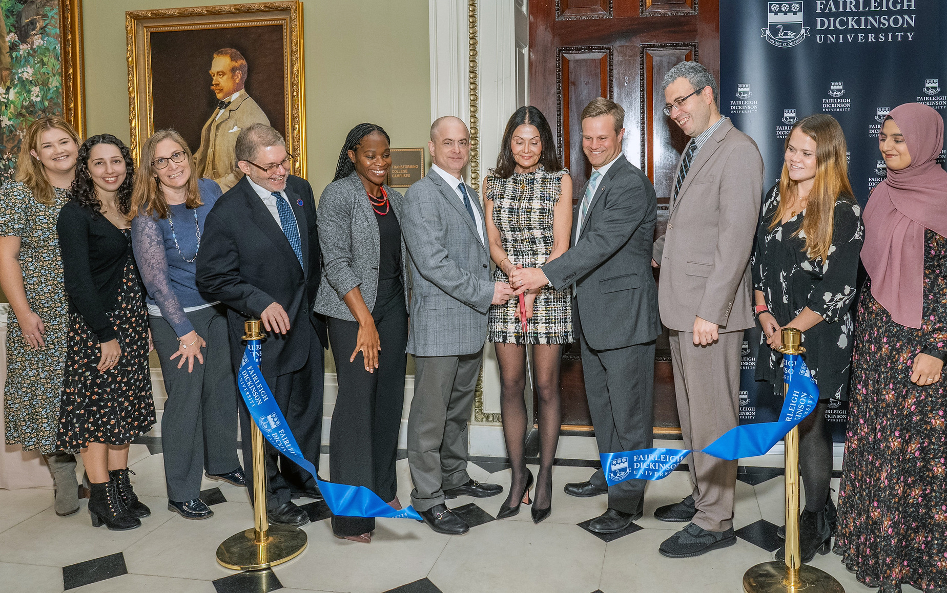 A group of men and women gather to cut a ribbon and officially dedicate a new office on campus.