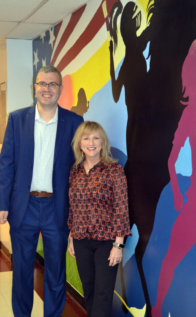 A man and a woman pose for a photo in front of a colorful mural.