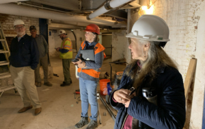 Three men and two women wearing hard hats stand in a construction site.