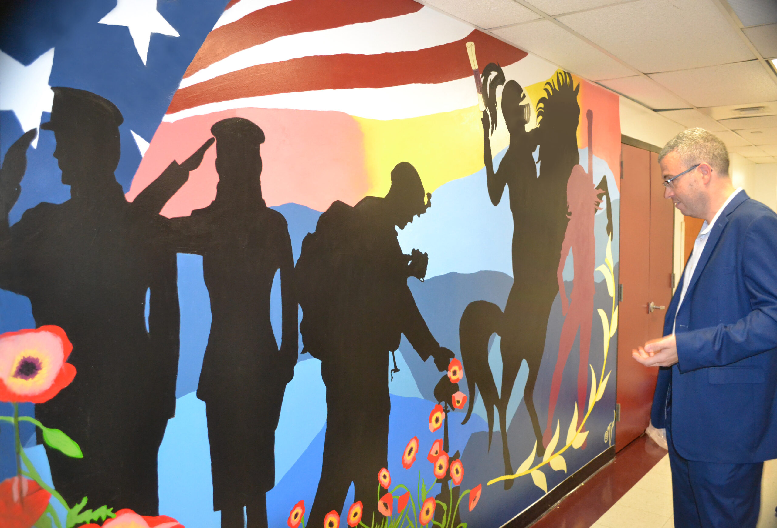 A mural depicts a veterans' journey. A man stands in front of the art, absorbing it.