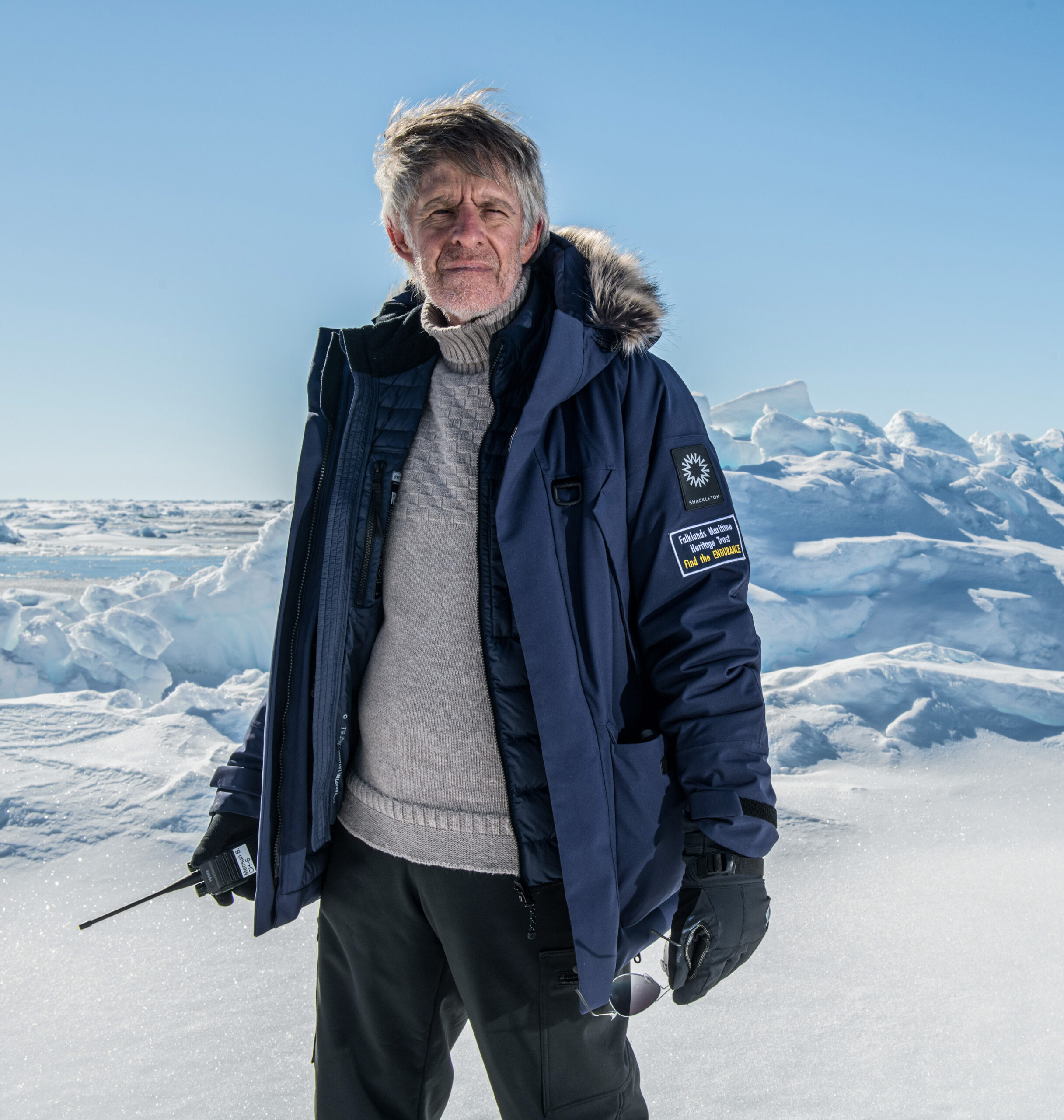 A man wearing a navy blue parka and heavy gloves, stands on the sea ice of the Weddell Sea in Antarctica.