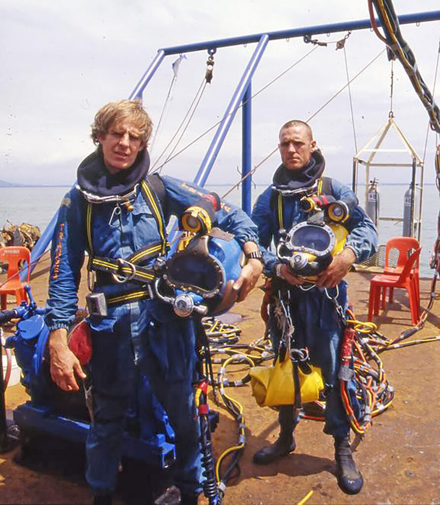 Two men dressed in scuba gear ready themselves for a dive.