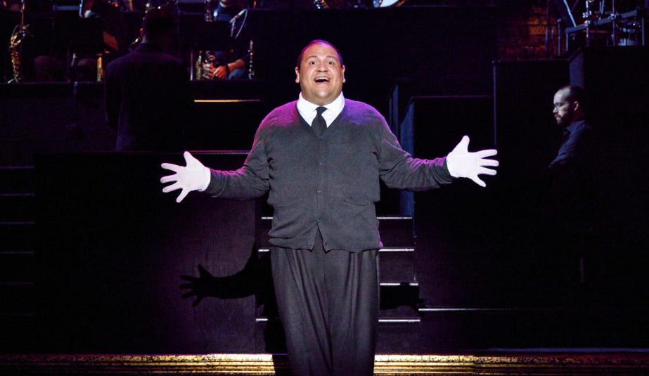 A man stands center stage, hands out, singing.