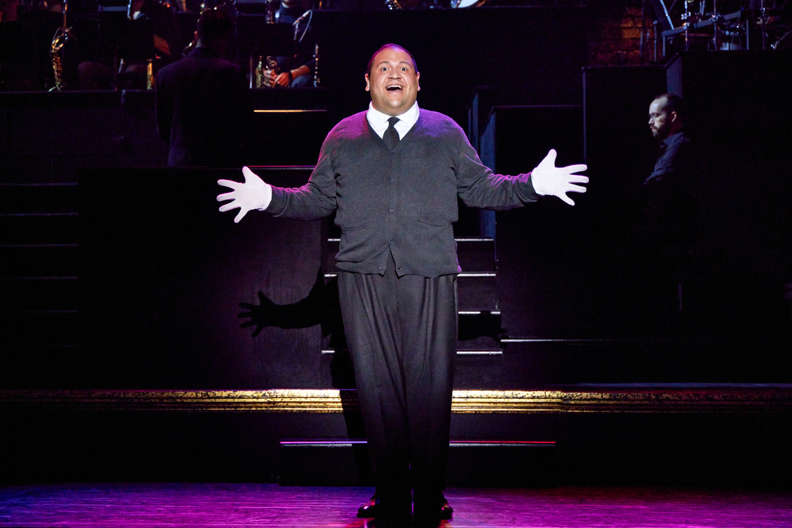 A man stands center stage, hands out, singing.