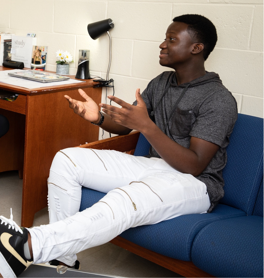 a student sitting on a couch. they speak to someone out of frame.