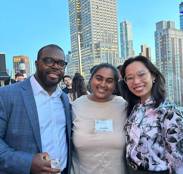 Three alumni, one man and two women, pose for a photo at a rooftop reception.