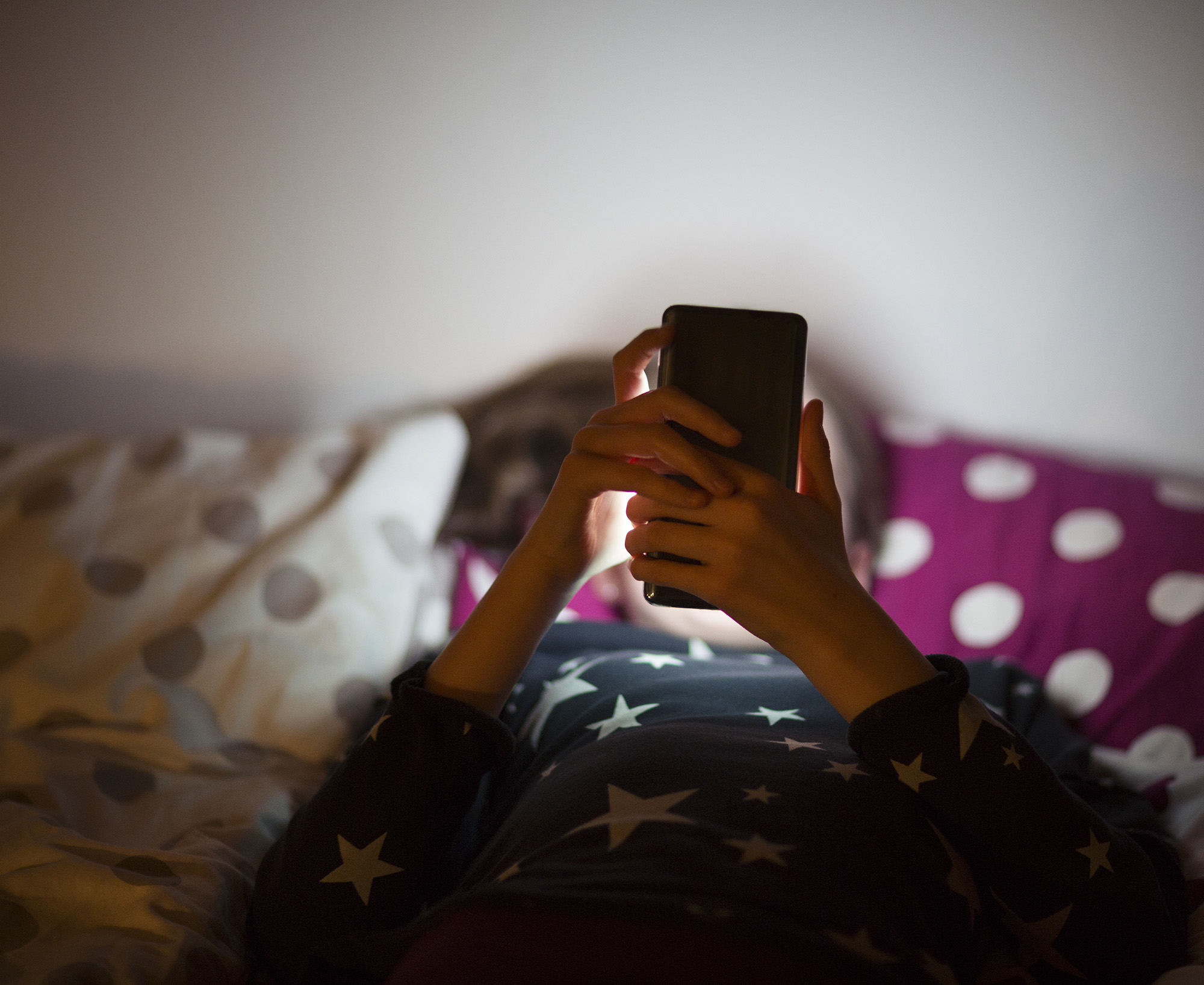 A young woman relaxes on a bed, and scrolls through her smartphone.