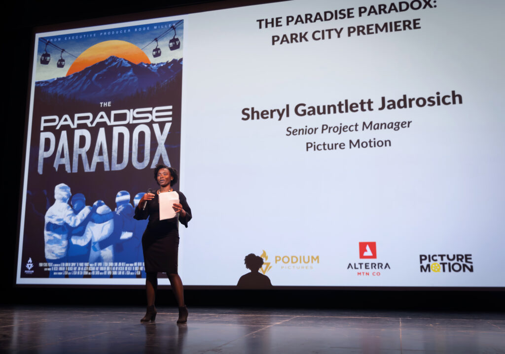 A woman on stage speaks into a microphone at a documentary screening.