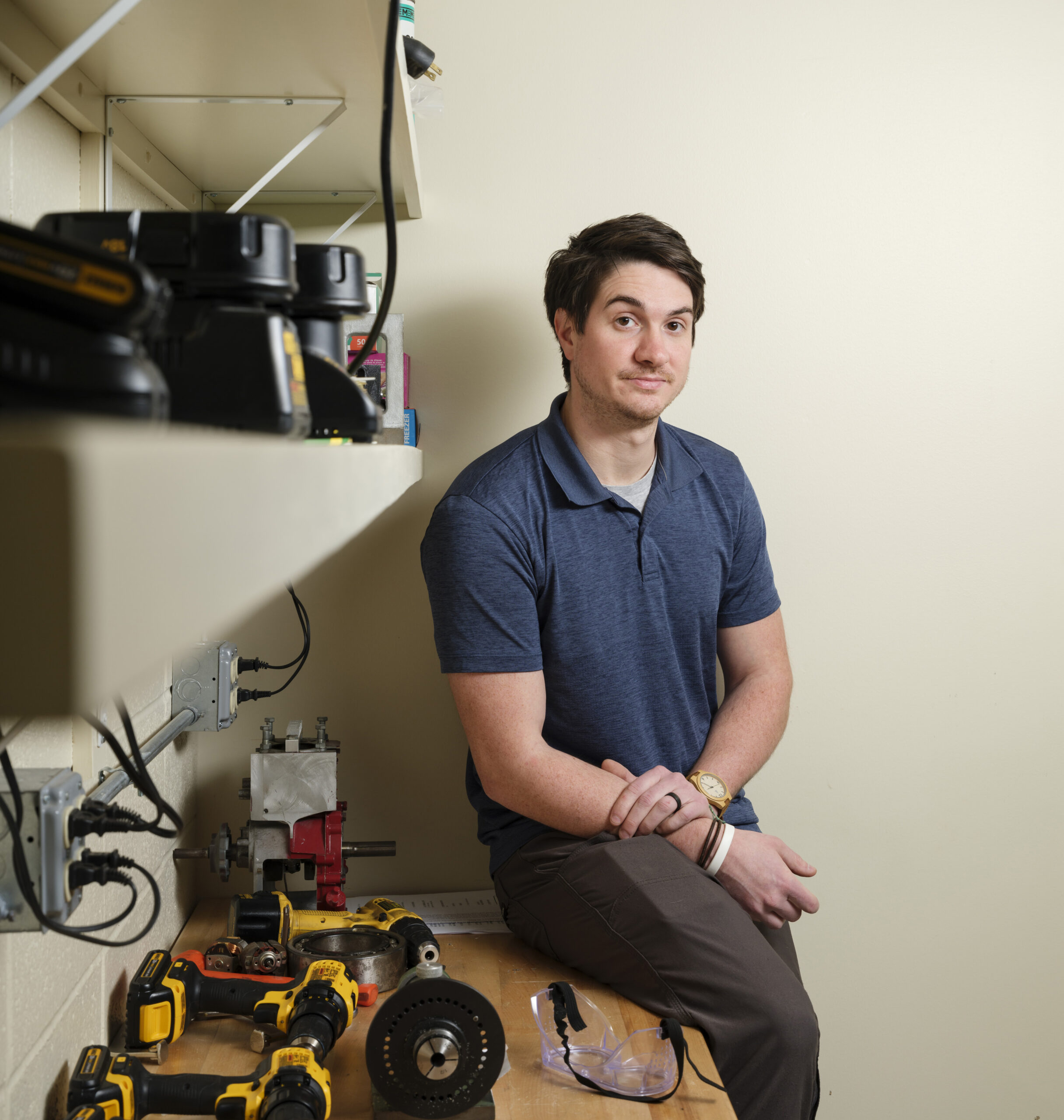 A man sits on the edge of a table next to various electronic devices and tools.