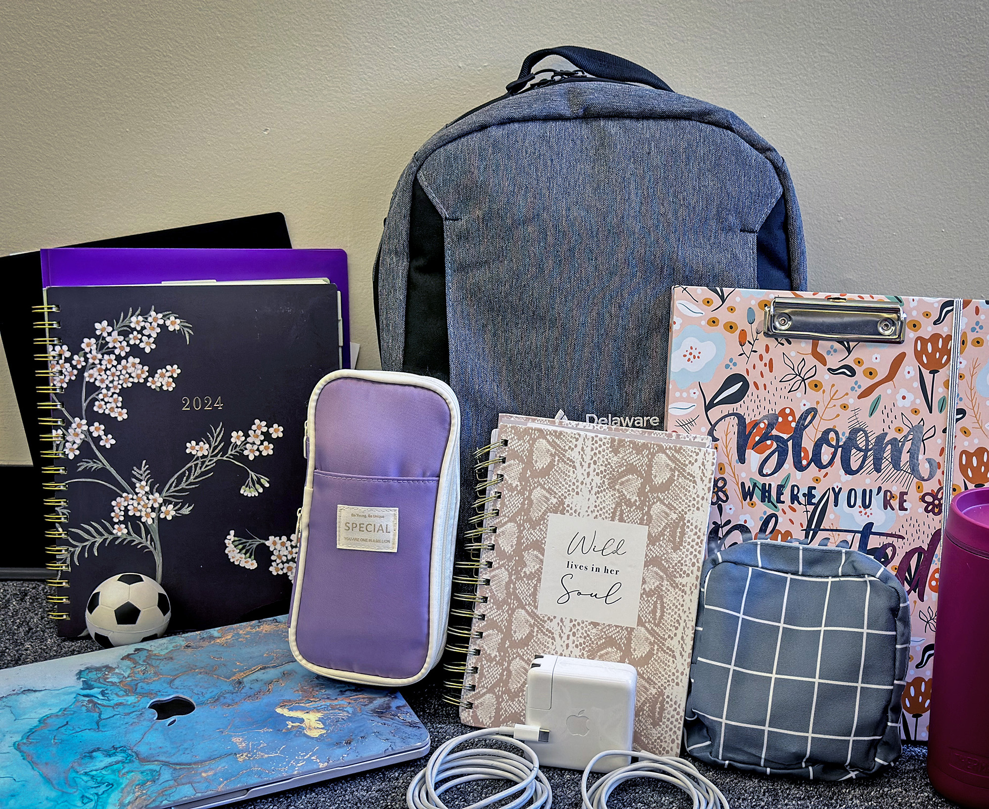 A laptop, a purple pouch, a planner, chargers, a gray backpack and more school supplies grouped together.
