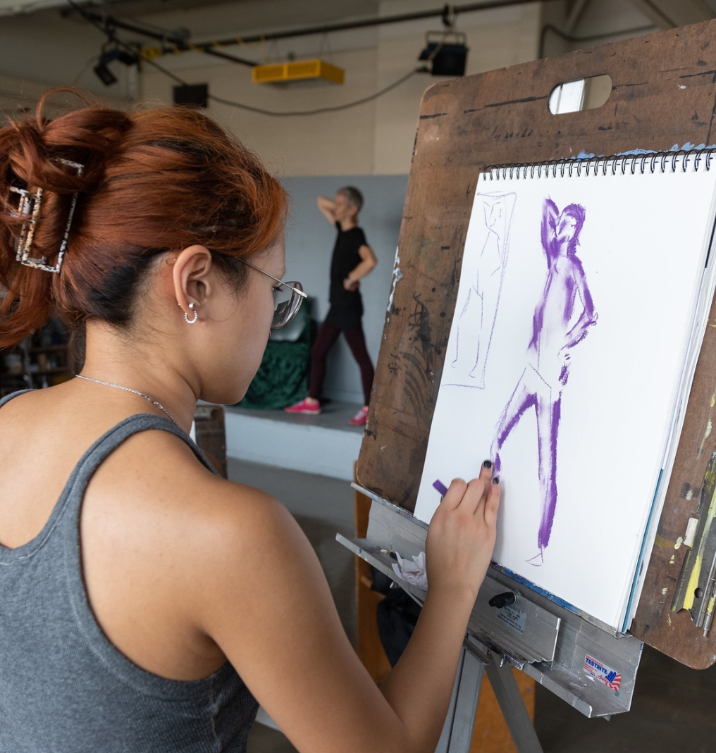 a student sketching based on a model in the background.