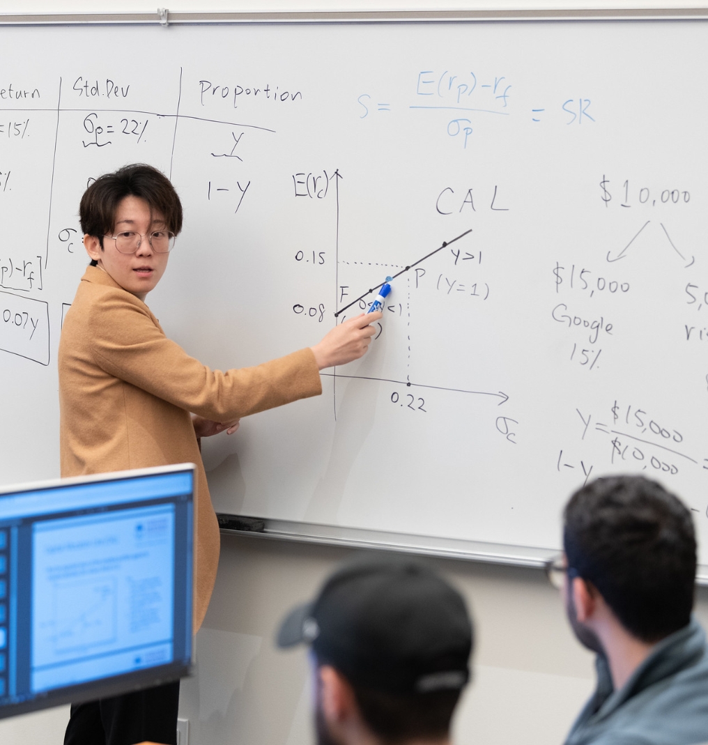 a teacher pointing to a diagram on a whiteboard. students watch.