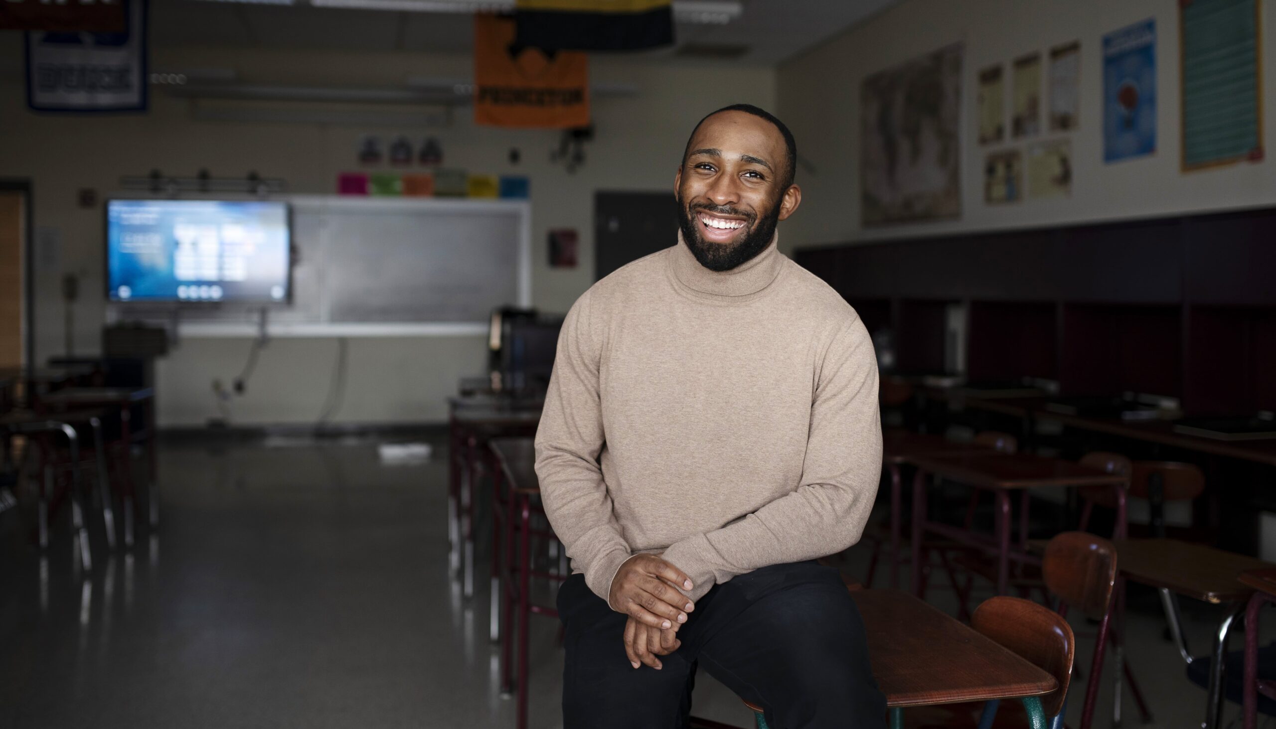 man in sweater stands in a classroom