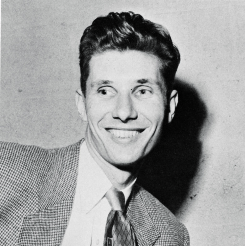 A head shot of a man smiling wearing a tie, dress shirt and suit jacket