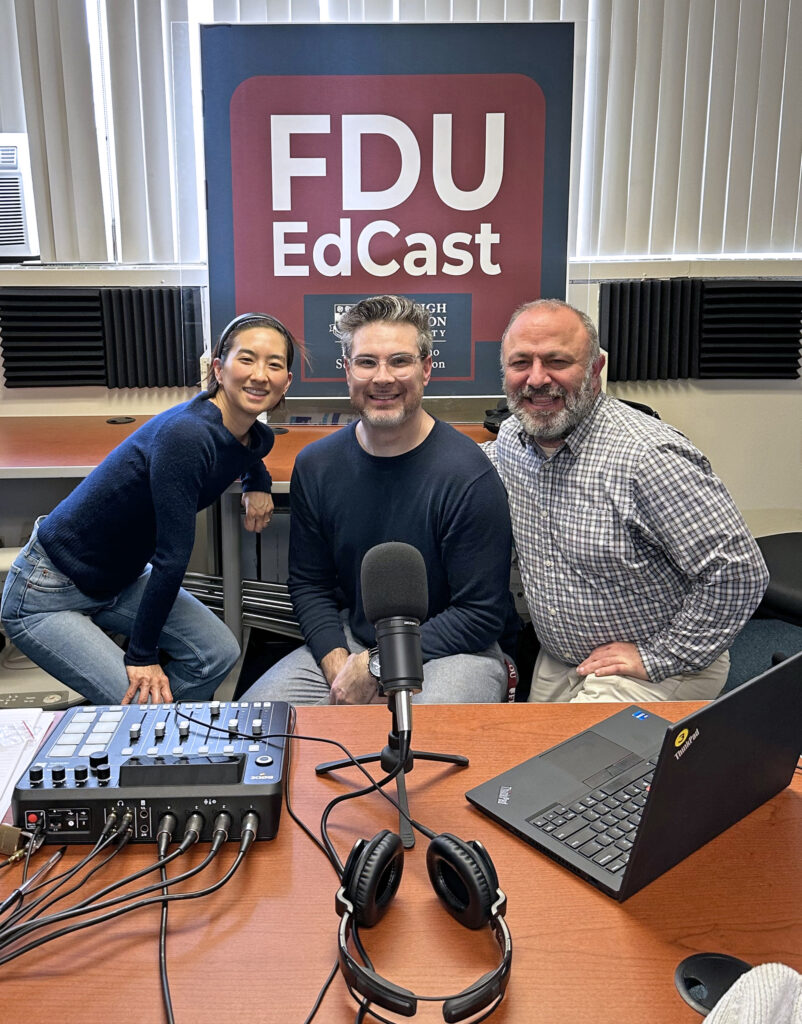 A woman and two men pose for a photo with podcast equipment in front of them.