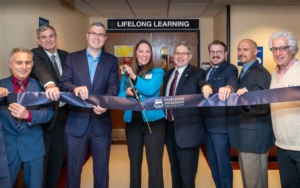 people posed with a ribbon at official event. the sign behind them reads "lifelong learning."