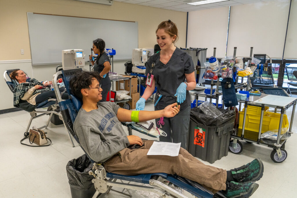 a student in a chair taking his blood taken. a nurse smiles over him.