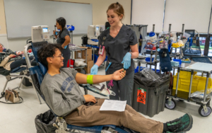 a student in a chair taking his blood taken. a nurse smiles over him.