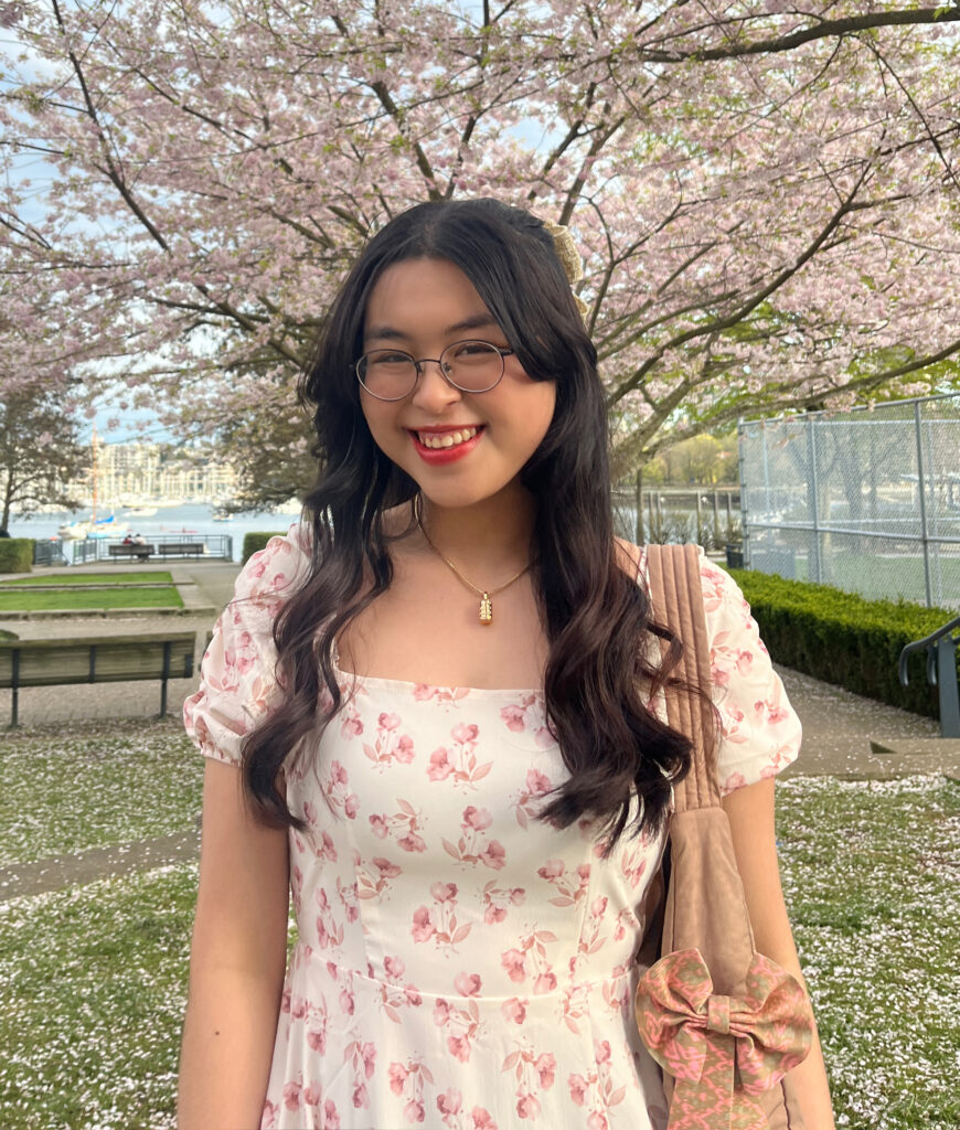 A young woman stands outside, in front of blooming trees.