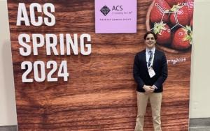 student stands in front of backdrop that reads "ACS Spring 2024"