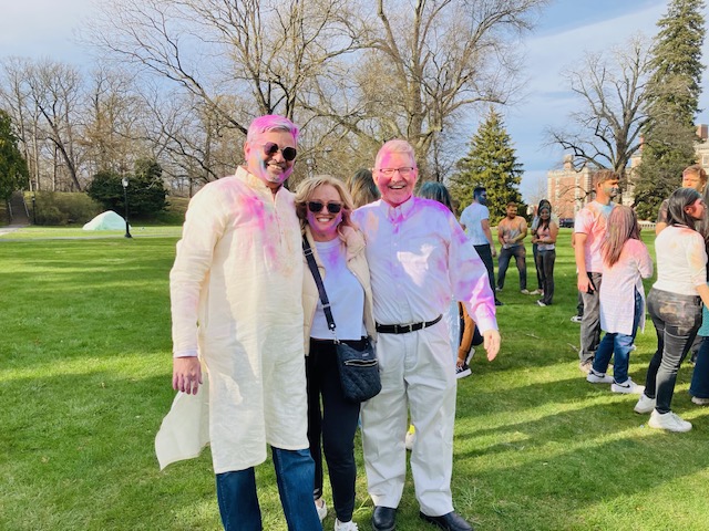 Three people stand together covered in pink powder celebrating Holi. 