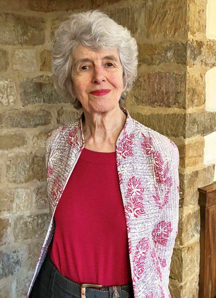 A woman with gray hair poses in front of a column of interior bricks at Wroxton Abbey.