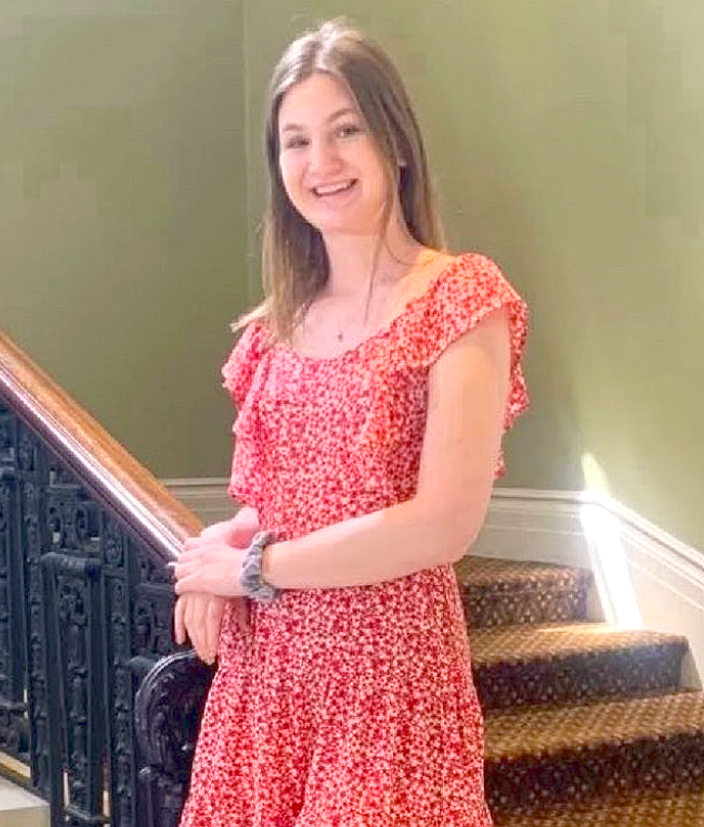 A young woman wearing a red dress leans against a wrought iron staircase banister.