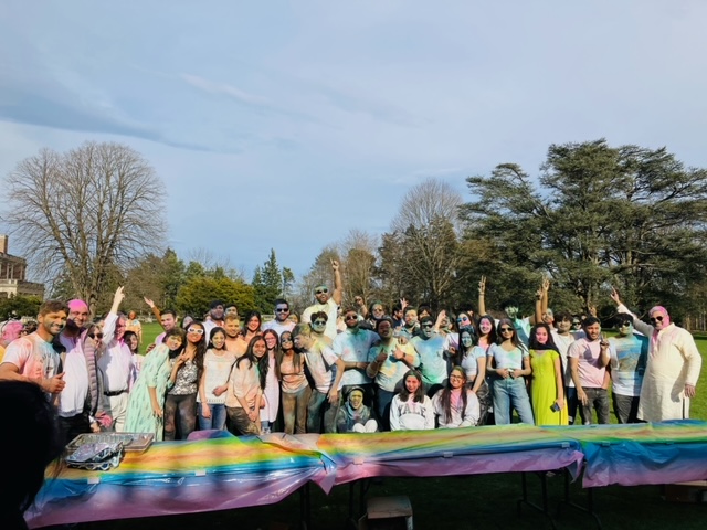 A group gathers together for a photo covered in multi-colored powder. 