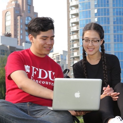 Three students sitting on the lawn looking at a laptop