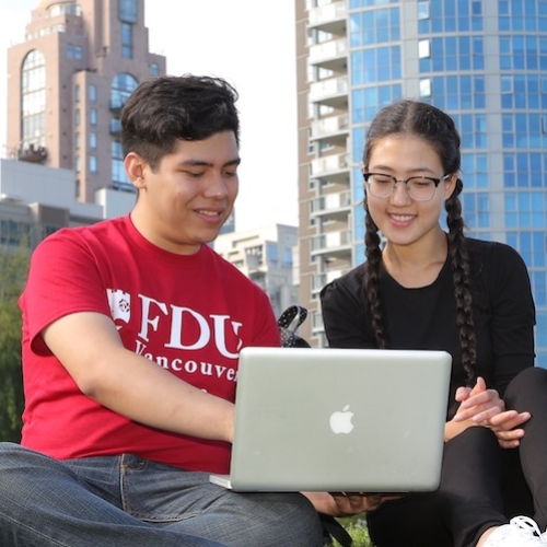 Three students sitting on the lawn looking at a laptop